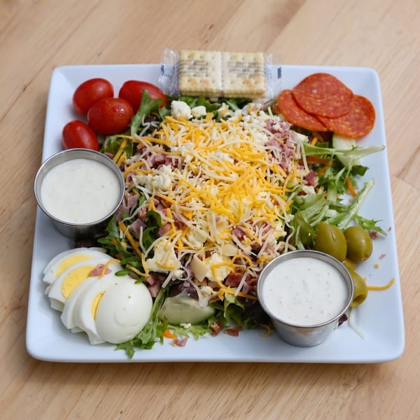 A large chef salad with cheese, pepperoni, tomatoes, olives, and hard-boiled eggs.