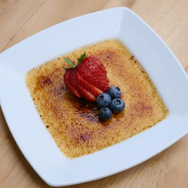 Crème brûlée with a caramelized sugar topping, garnished with a fresh strawberry and blueberries.
