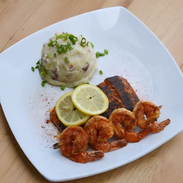 Grilled salmon and shrimp with lemon slices and a side of mashed potatoes, garnished with chives.