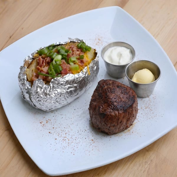 Grilled steak with a loaded baked potato, sour cream, and butter on a white plate.