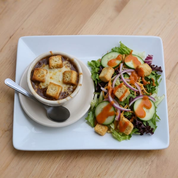 French onion soup with melted cheese and croutons, served with a side salad on a white plate.